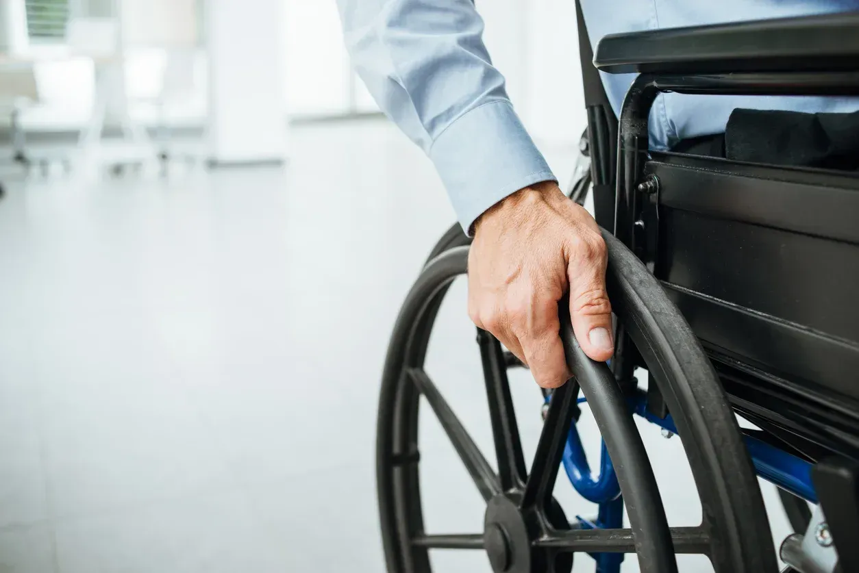 Person in a wheelchair, close up of hand on the wheel, indoors in an office setting.