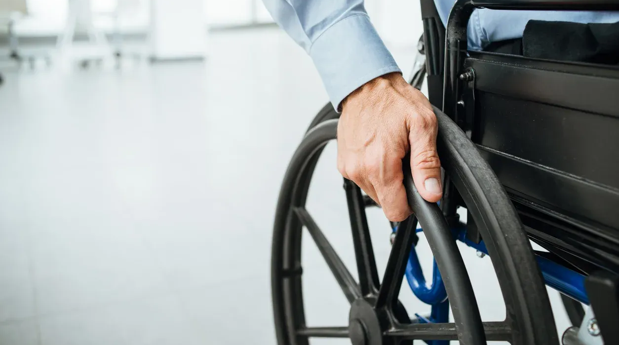 Person in a wheelchair, close up of hand on the wheel, indoors in an office setting.