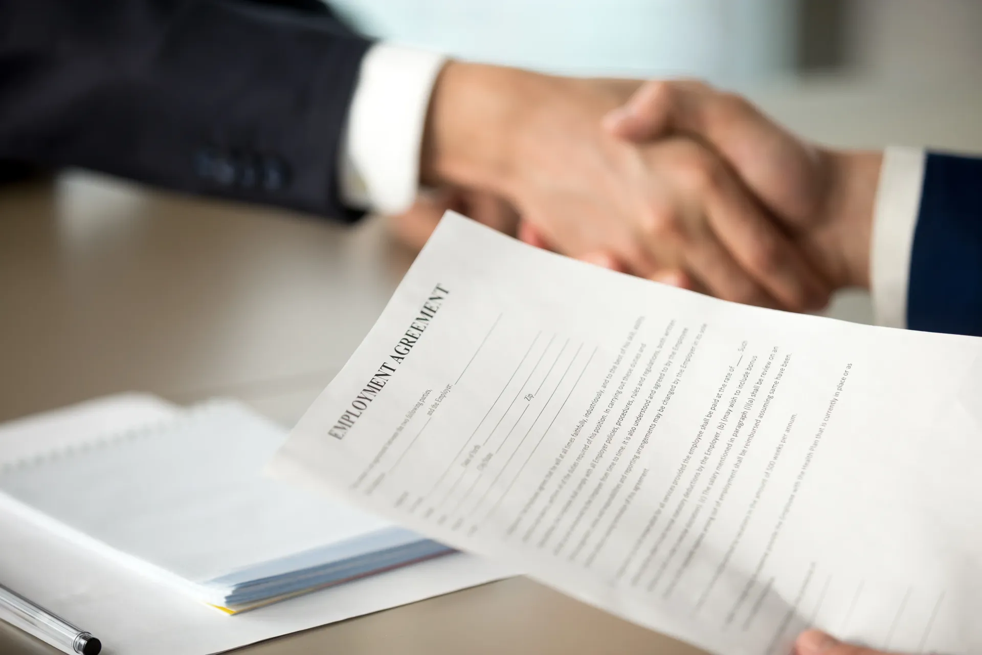 Two people are shaking hands over an employment contract.