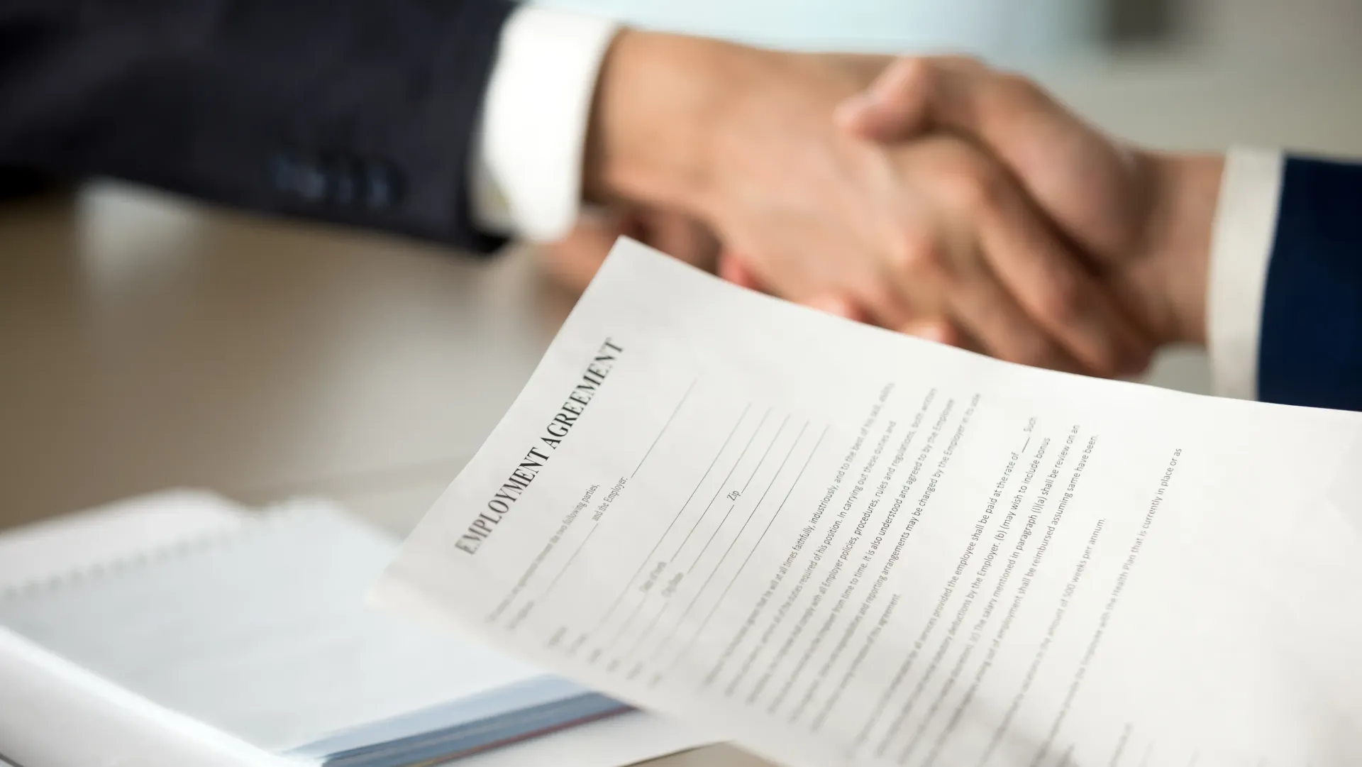 Two people are shaking hands over an employment contract.