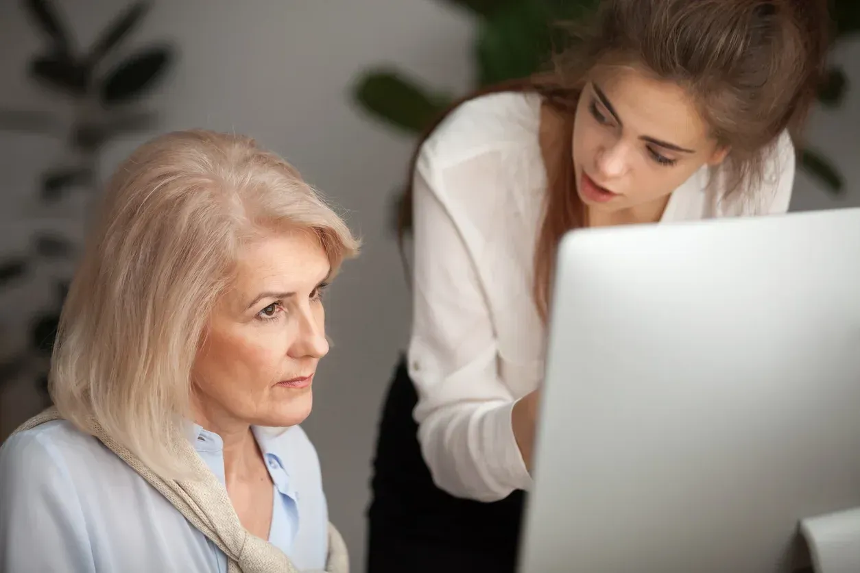 Older woman and younger woman look at computer screen. The younger woman points.