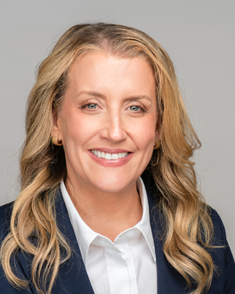 A woman in a blue jacket and white shirt is smiling for the camera.