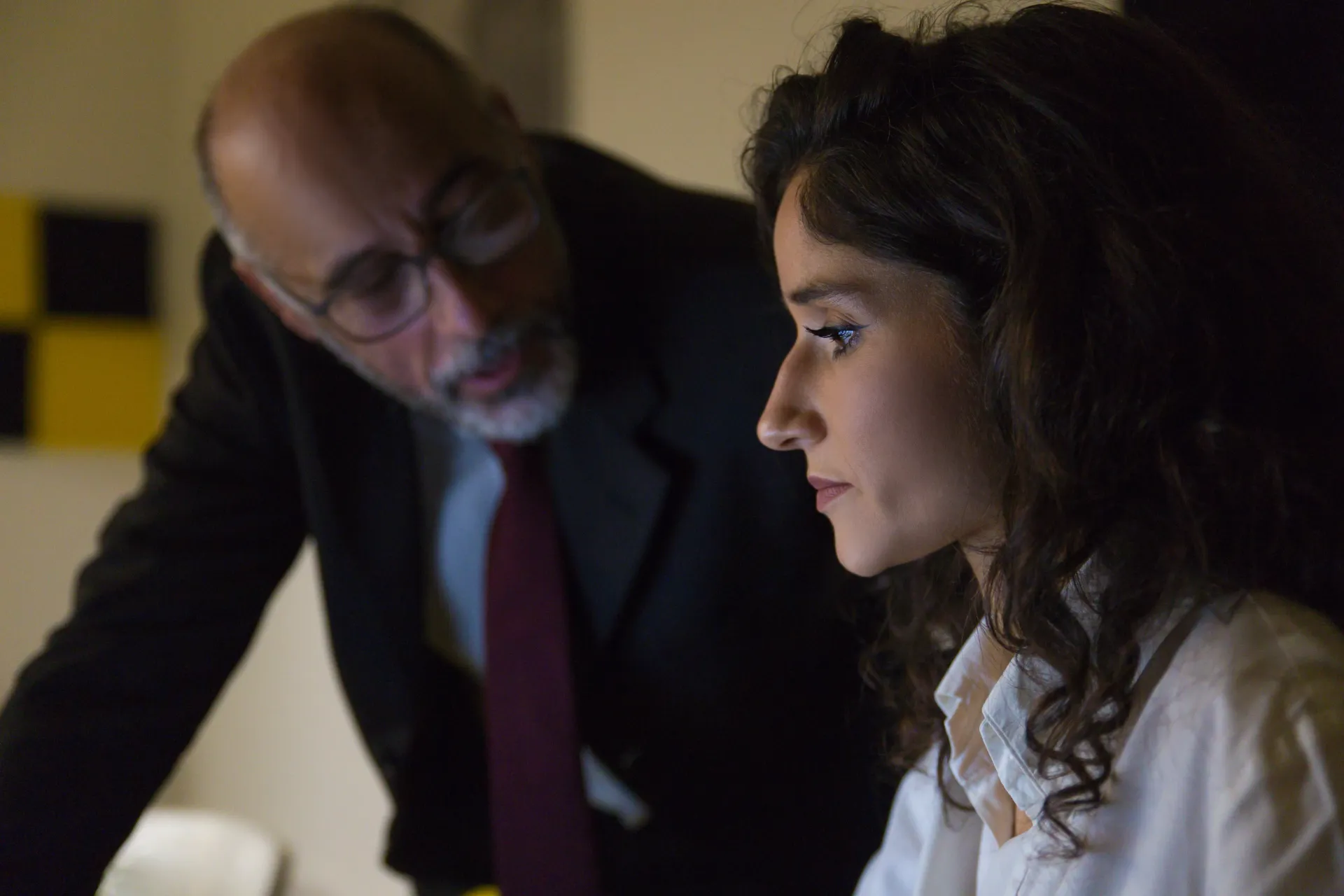 A man and a woman are working at a computer. The man is looking at her.