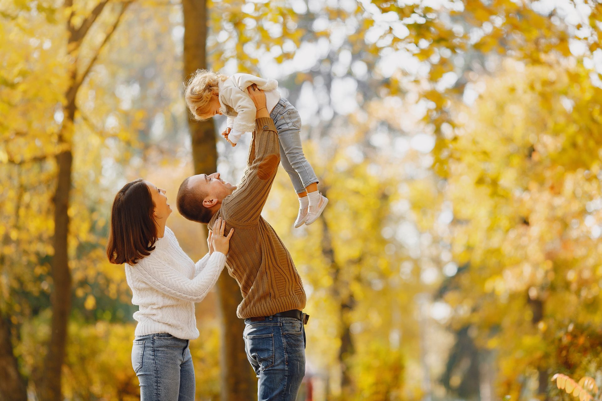 A man and woman are holding a baby in the air in a park.