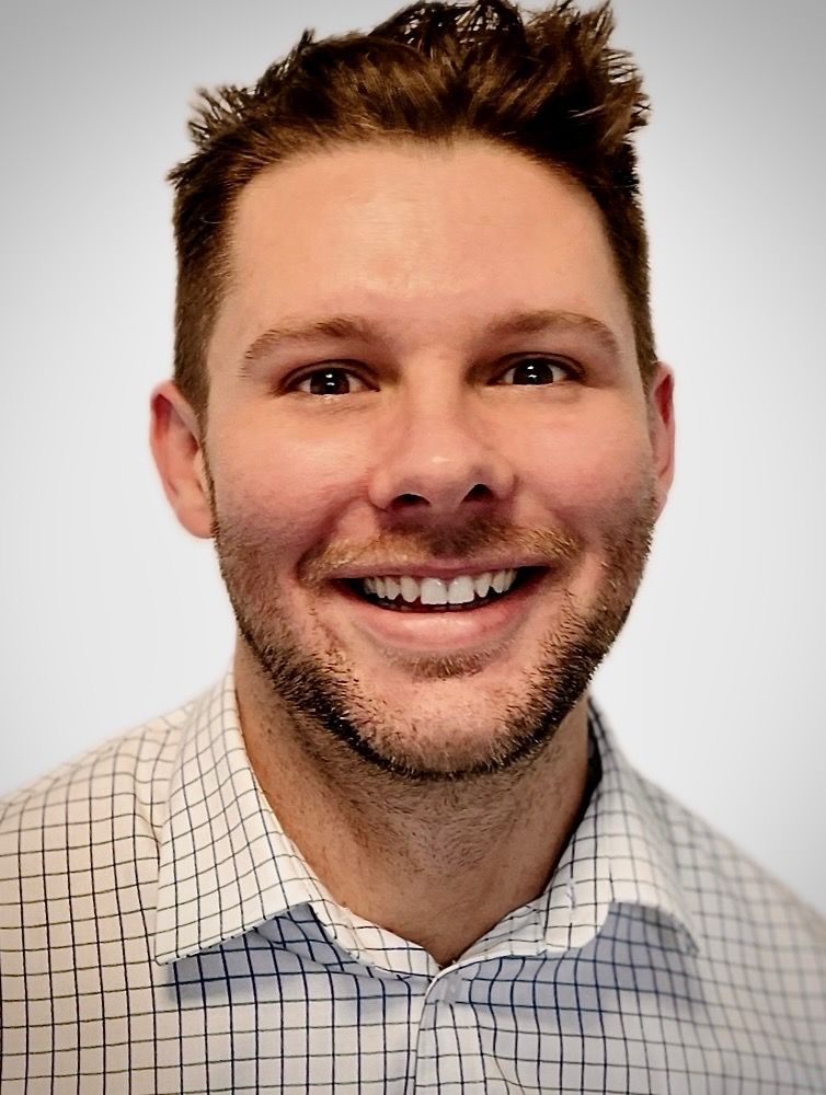A man with a beard is smiling and wearing a plaid shirt