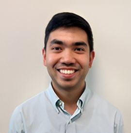 A man in a light blue shirt is smiling for the camera.