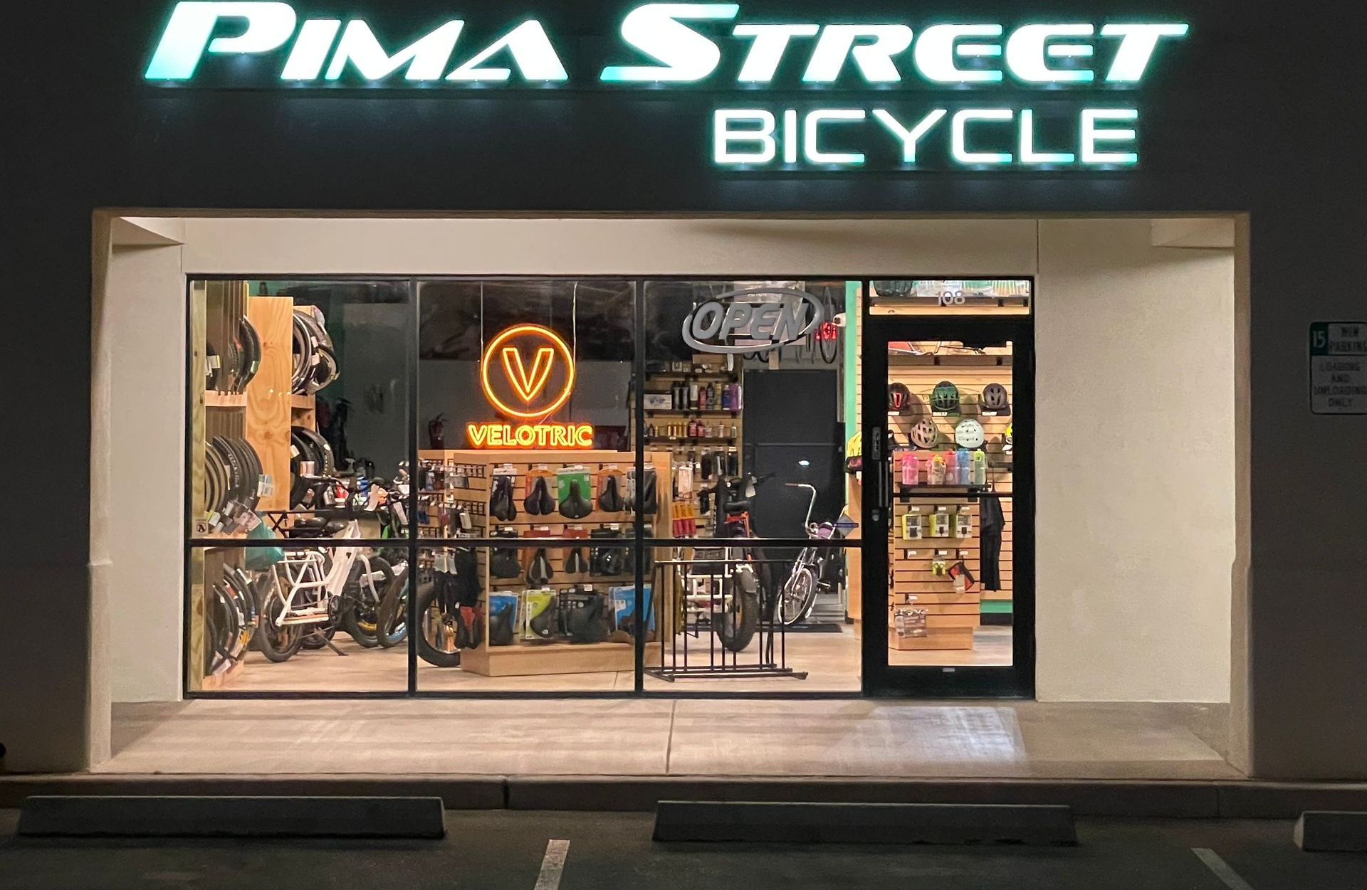 Pima Street Bicycle shop storefront at night with bright neon sign and bikes visible inside