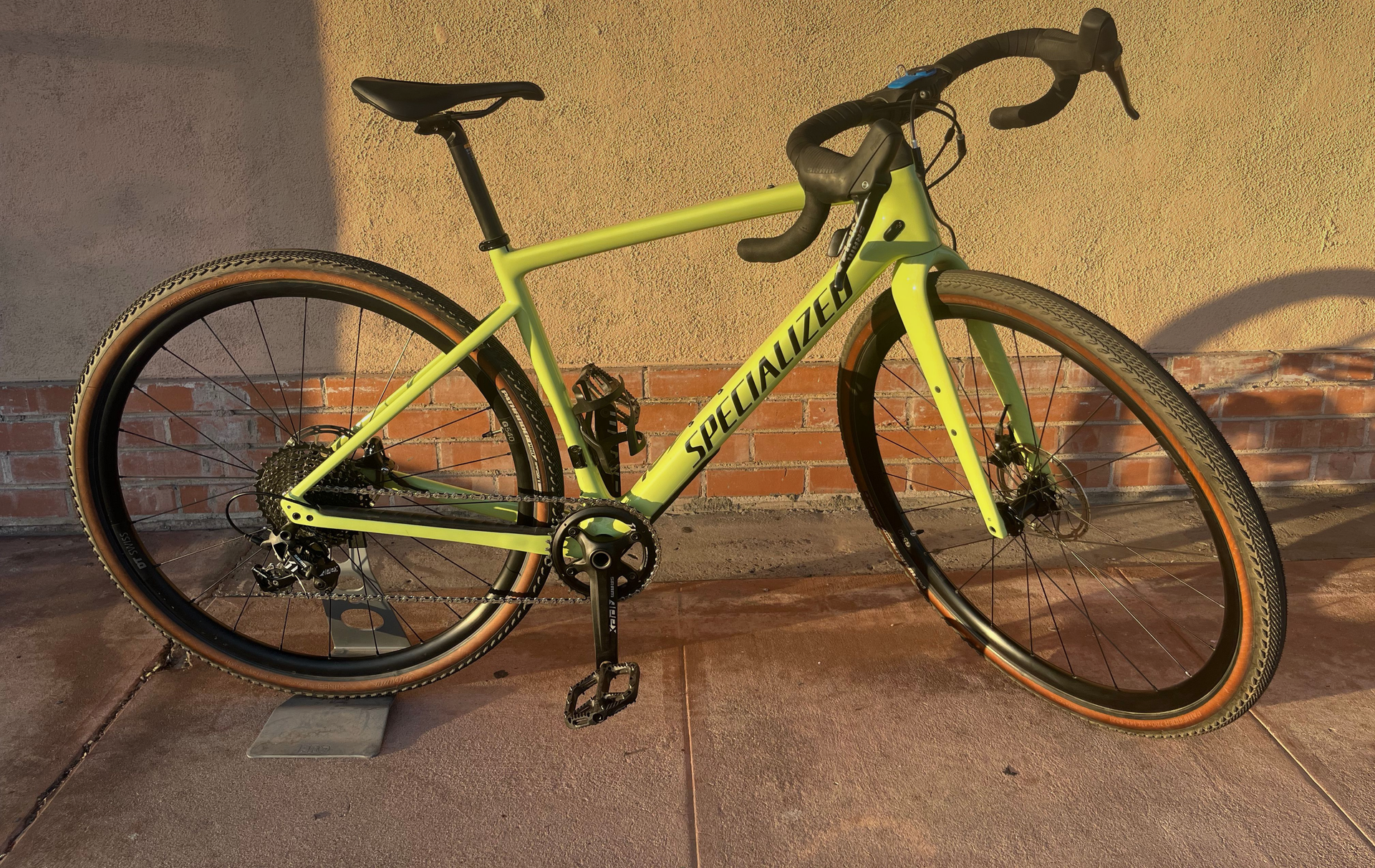 Green Specialized gravel bike leaning against a tan wall, casting a shadow.