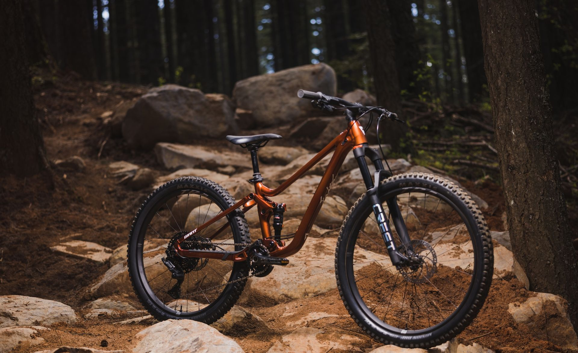 Orange mountain bike on a rocky trail in a forest, surrounded by trees.