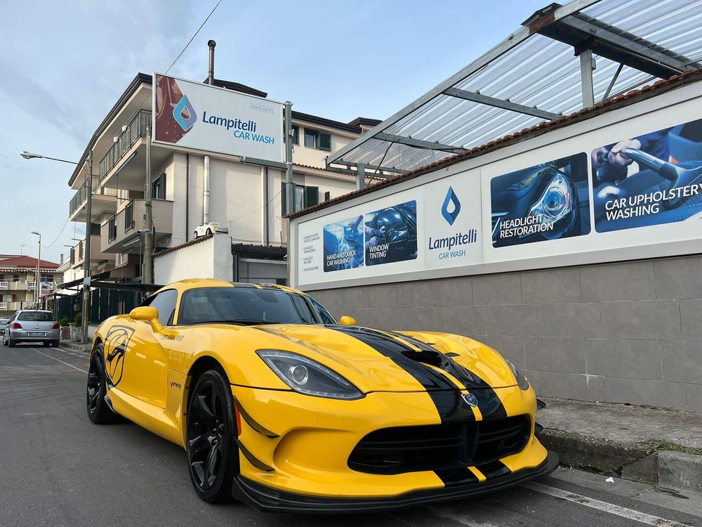 Un'auto sportiva Dodge Viper gialla con strisce nere parcheggiata in strada. Sullo sfondo un edificio.