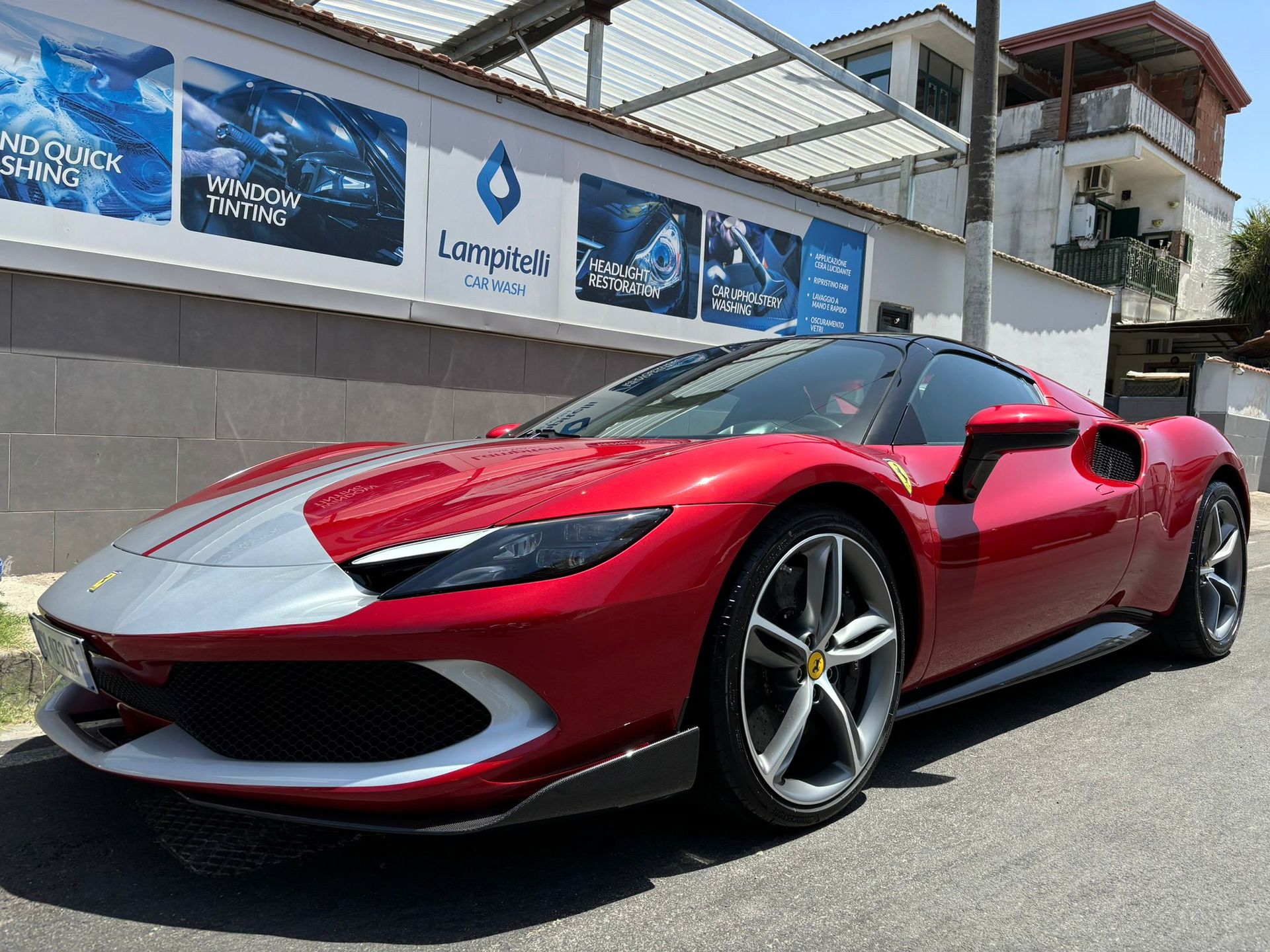 Un'auto sportiva Ferrari rossa parcheggiata su una strada, con una striscia da corsa argentata sul cofano, davanti a un edificio.