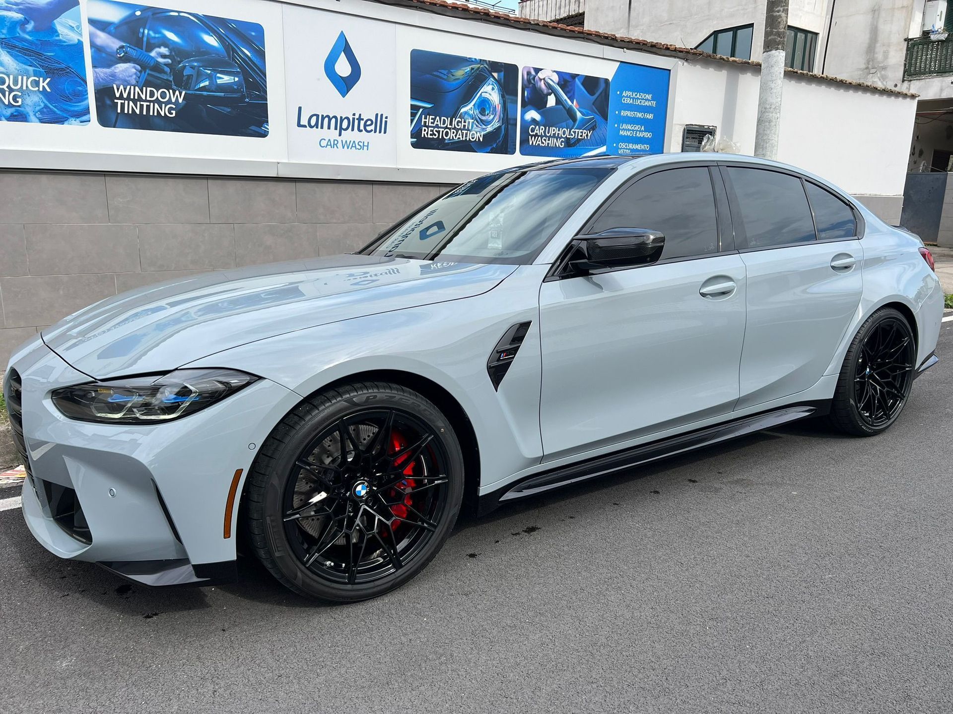 Berlina BMW M3 grigia con cerchi neri e pinze dei freni rosse parcheggiata su una strada.