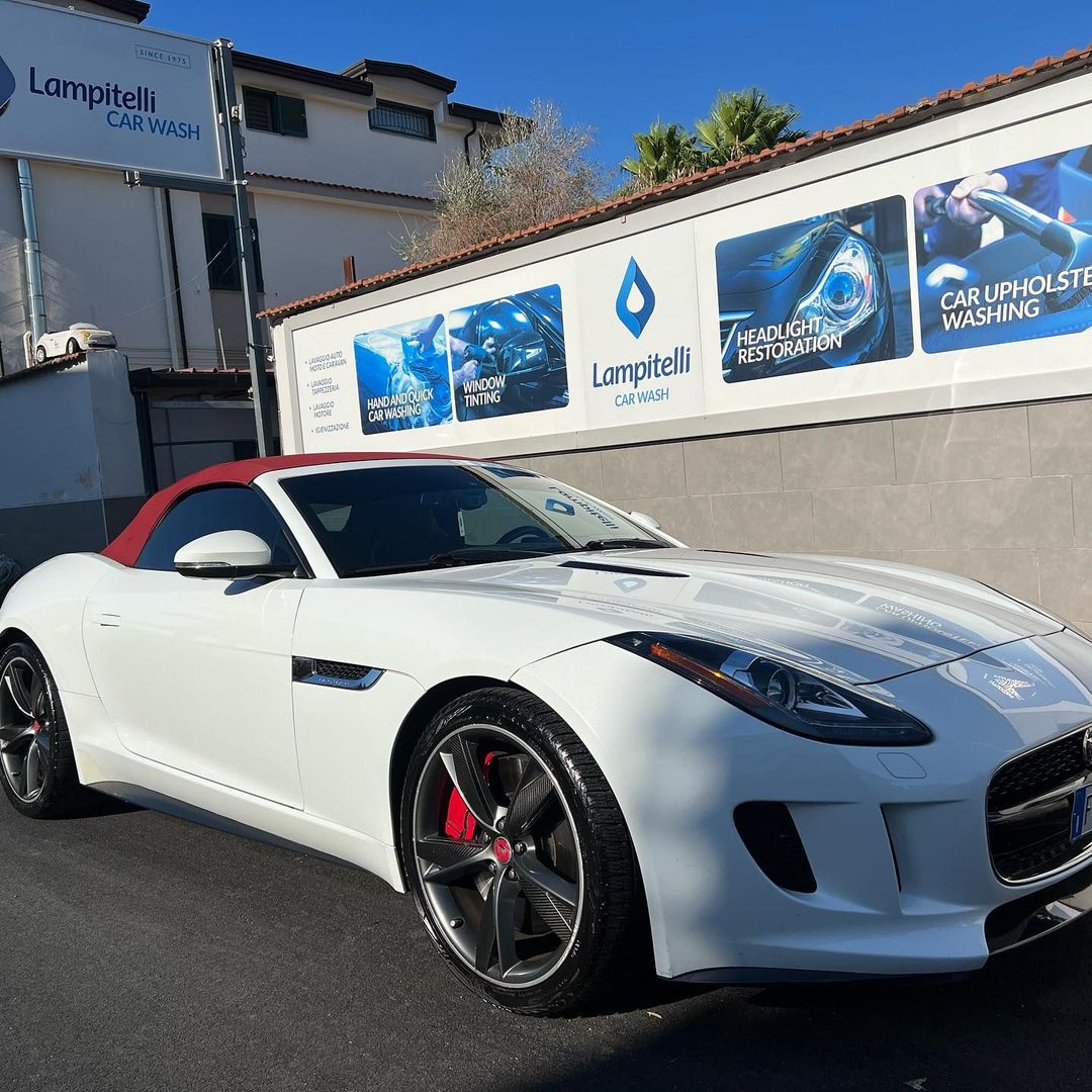 Una Jaguar bianca decappottabile parcheggiata in un autolavaggio con il tetto rosso e le pinze dei freni rosse.