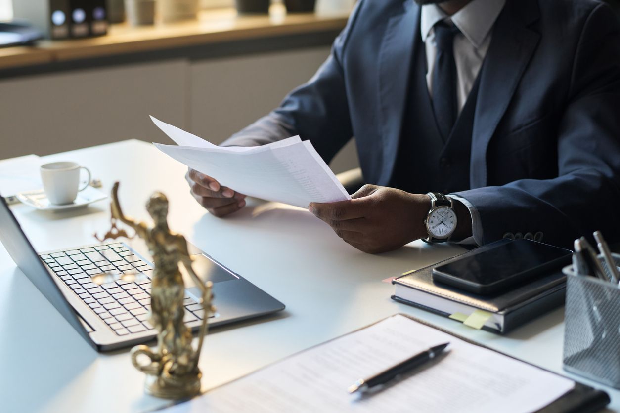 Businessman reviewing documents at an office desk with a laptop, coffee cup, and statue figurine.
