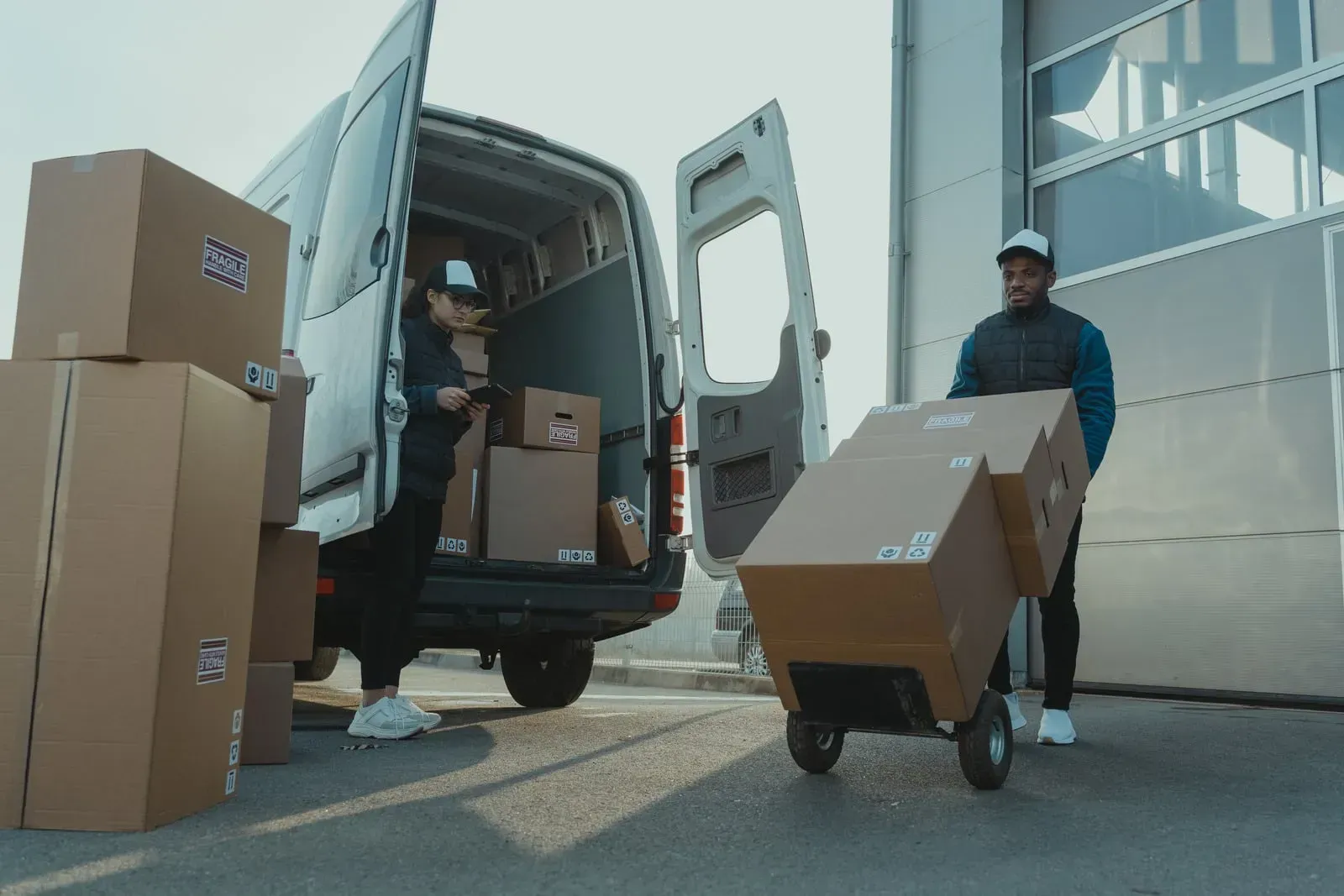 Two movers loading cardboard boxes into a white delivery van outside a building