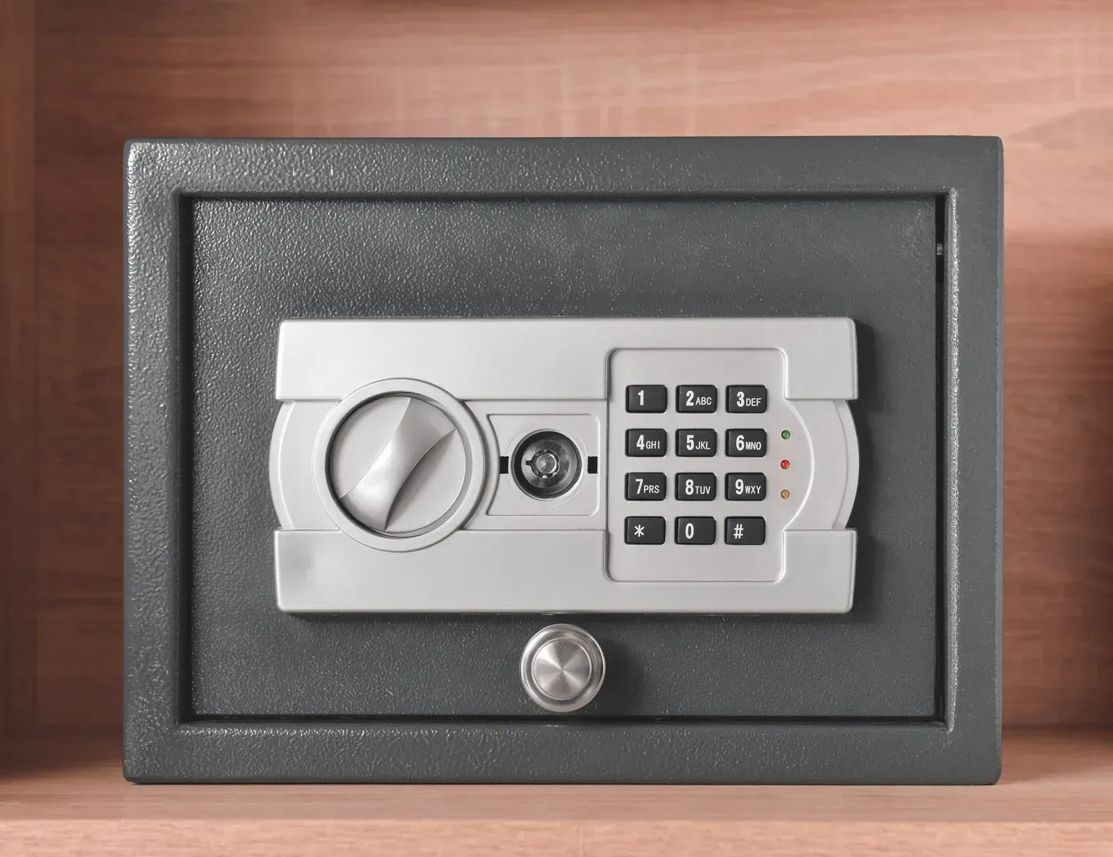 Gray digital safe door with keypad and combination lock on a wooden surface