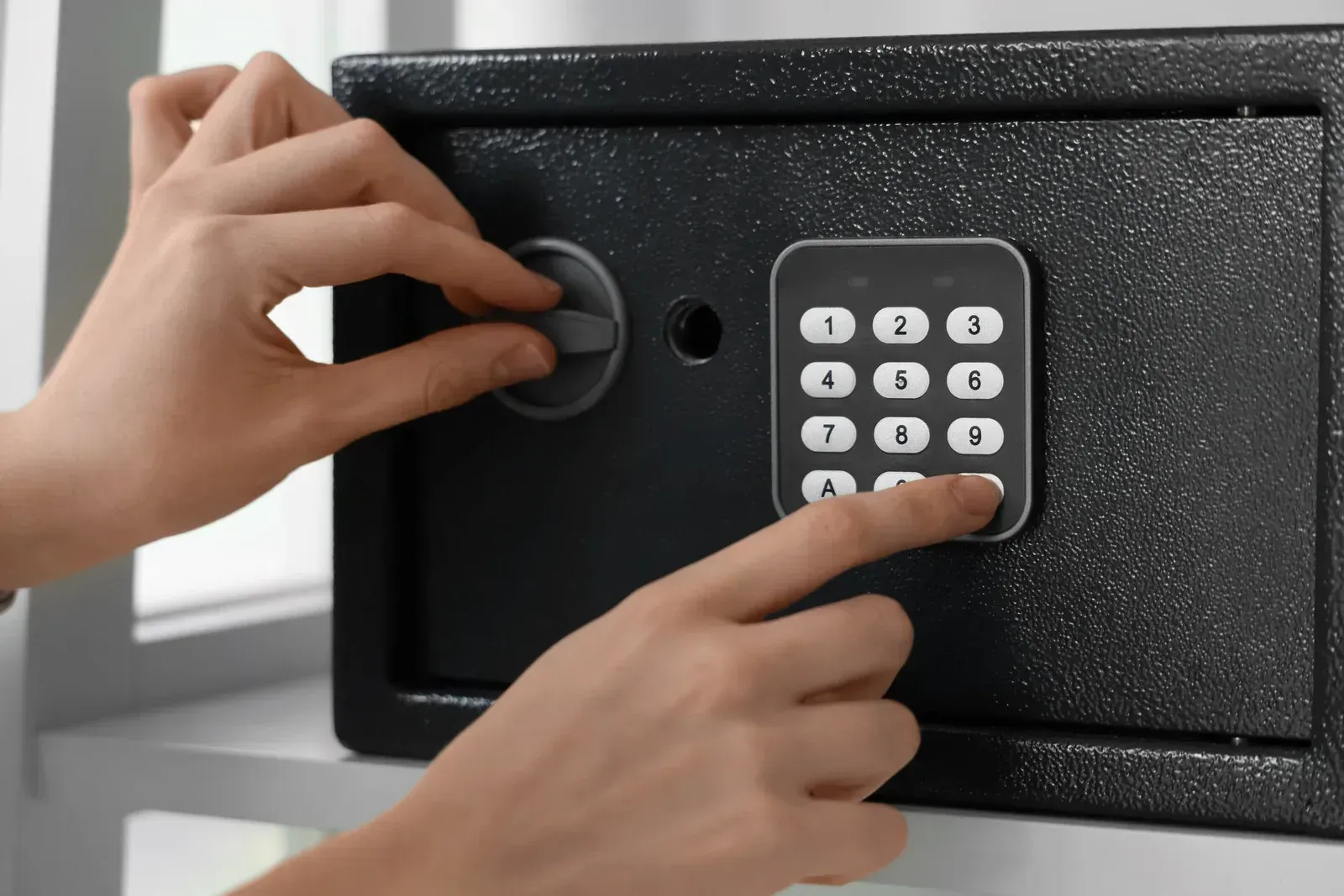 Hands entering a black safe using a keypad and dial lock