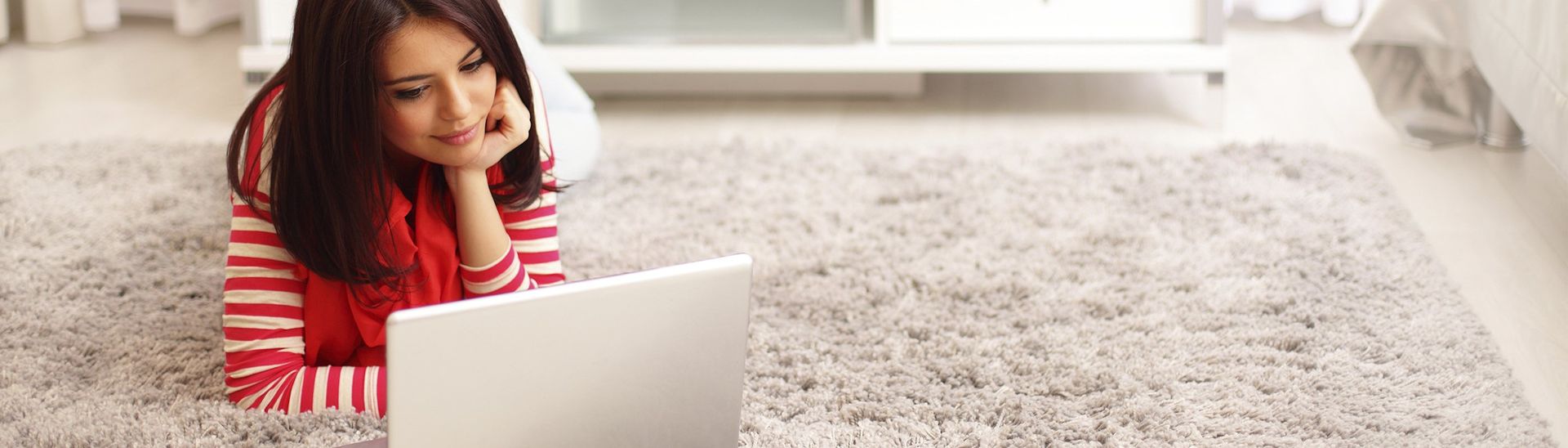 Woman lying on a carpet looking at her laptop