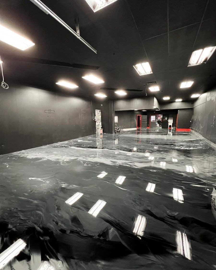Black-walled, empty room with reflective, black flooring. Overhead fluorescent lights cast bright reflections.