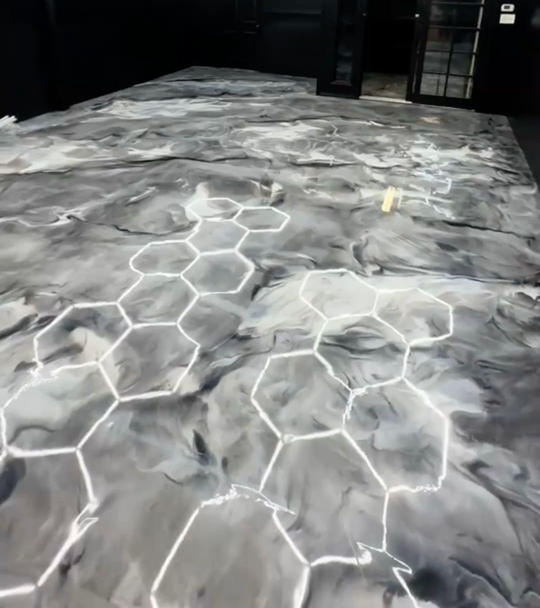 A glossy gray and white marbled floor featuring a pattern of glowing white hexagonal outlines set against a black room.