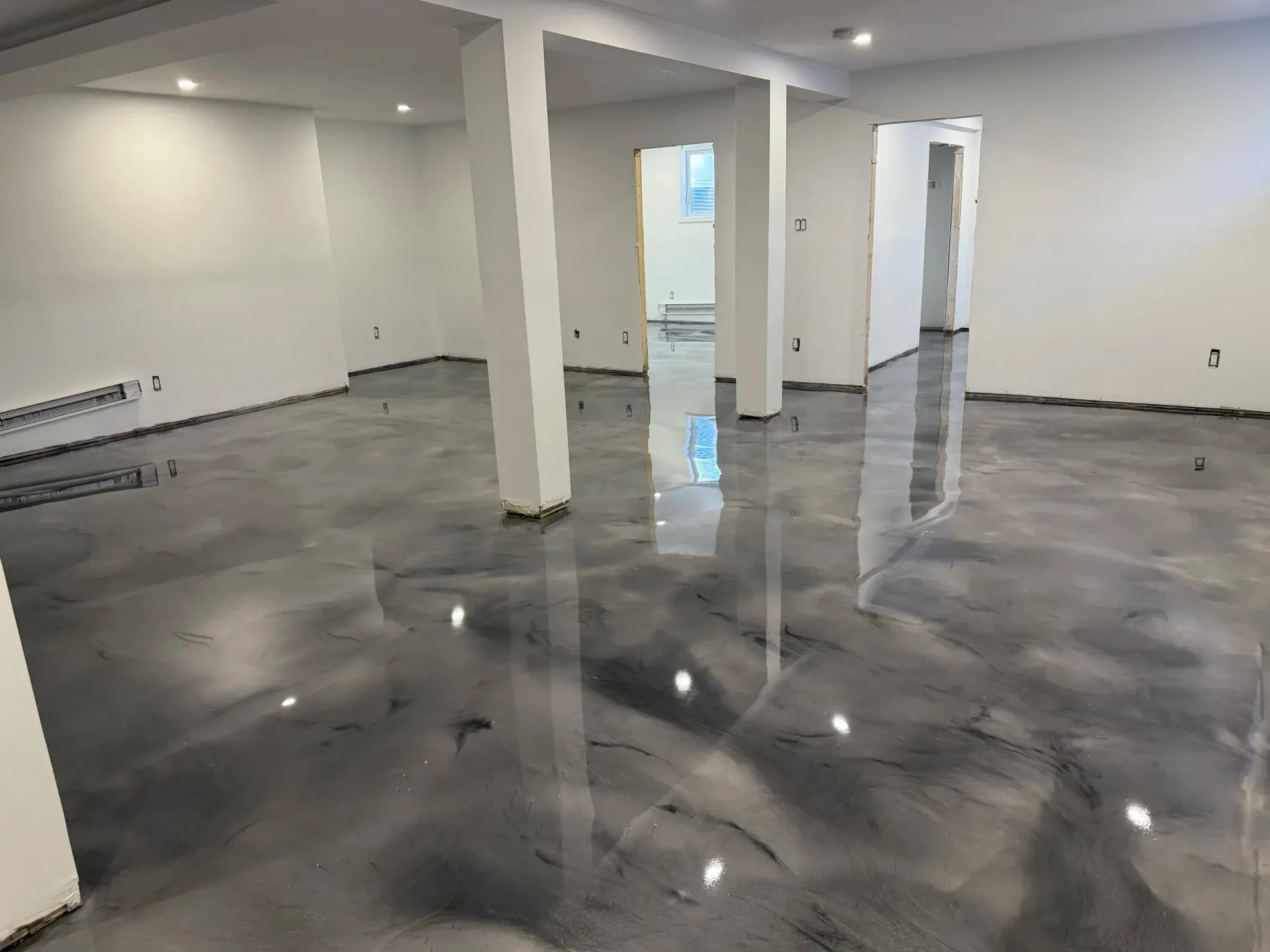 Open room with a shiny gray epoxy floor and white walls. Four white support columns are present.
