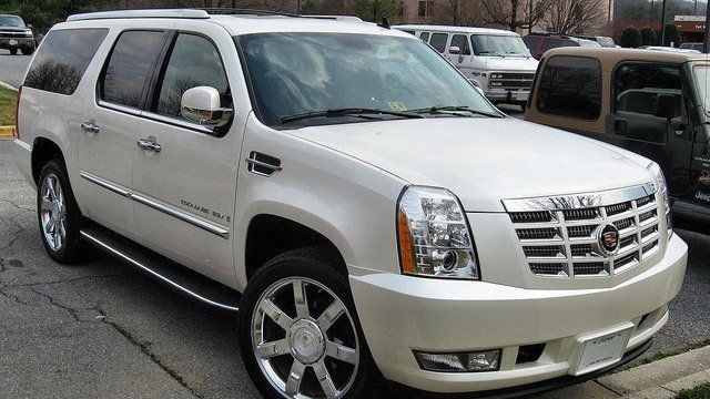 A white cadillac escalade is parked on the side of the road.