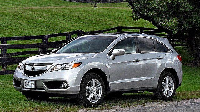 A silver car is parked on the side of the road in front of a fence.