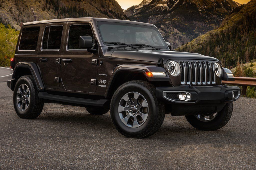 A black jeep wrangler is parked on the side of a road in front of mountains.