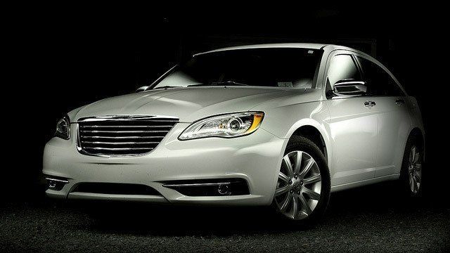 A white chrysler car is parked in the dark.