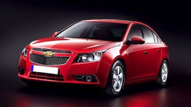 A red chevrolet cruze is parked on a dark surface.