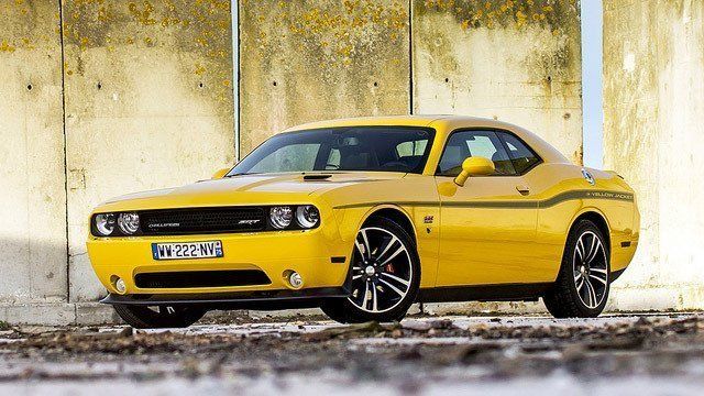 A yellow dodge challenger is parked in front of a concrete wall.