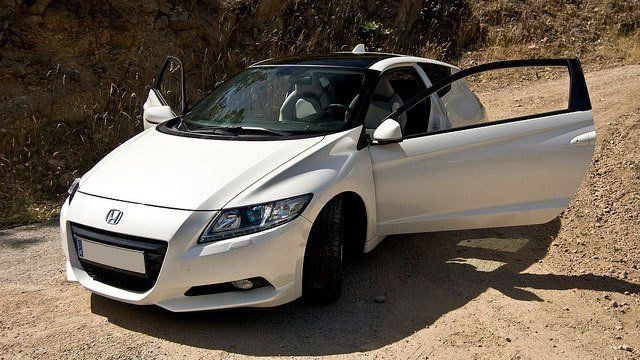 A white car is parked on a dirt road with its doors open
