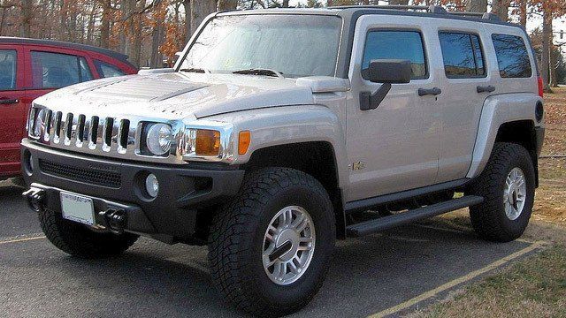 A white hummer is parked next to a red jeep in a parking lot.