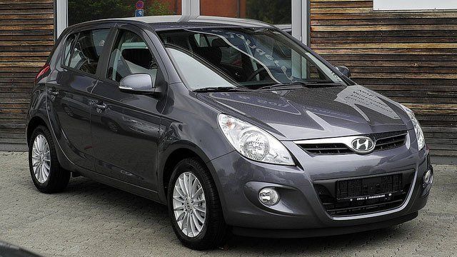 A gray car is parked in front of a wooden building.