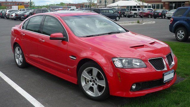 A red pontiac gto is parked in a parking lot.