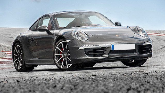 A gray porsche 911 is parked on a gravel road.