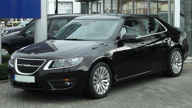 A black car is parked in front of a car dealership.