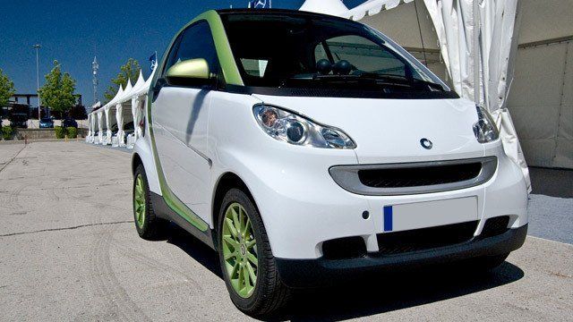 A white car with green wheels is parked in front of a white tent