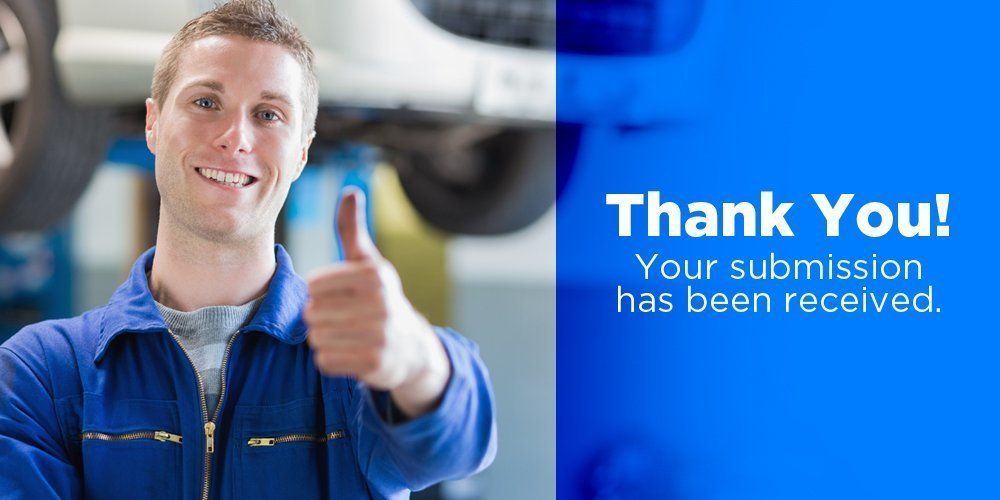 A man in a blue jacket is giving a thumbs up in a garage.