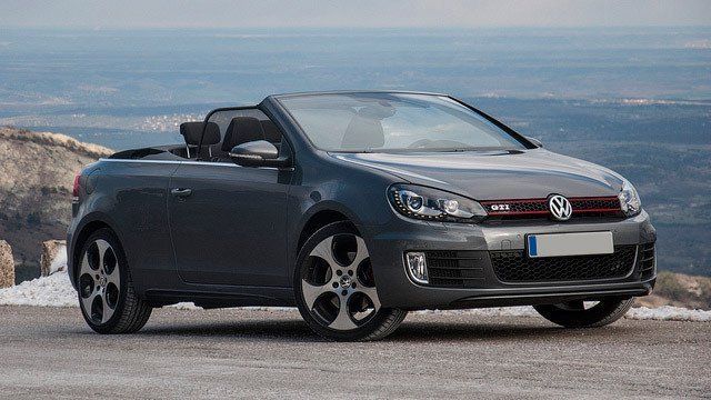 A volkswagen golf convertible is parked on the side of a road next to the ocean.