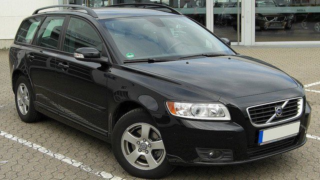 A black volvo is parked in a parking lot in front of a building.