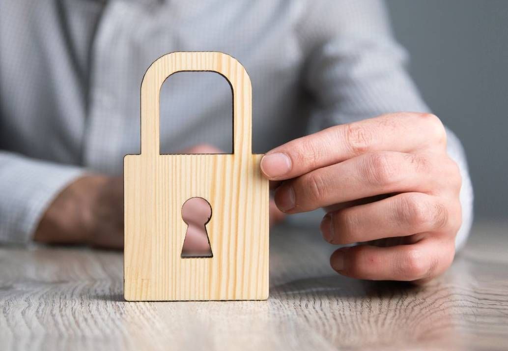 Persona che tiene in mano un lucchetto di legno su un tavolo, simbolo di sicurezza o protezione.