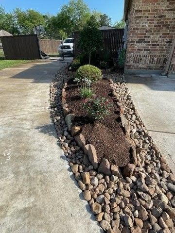 A garden with rocks and mulch in front of a brick house.