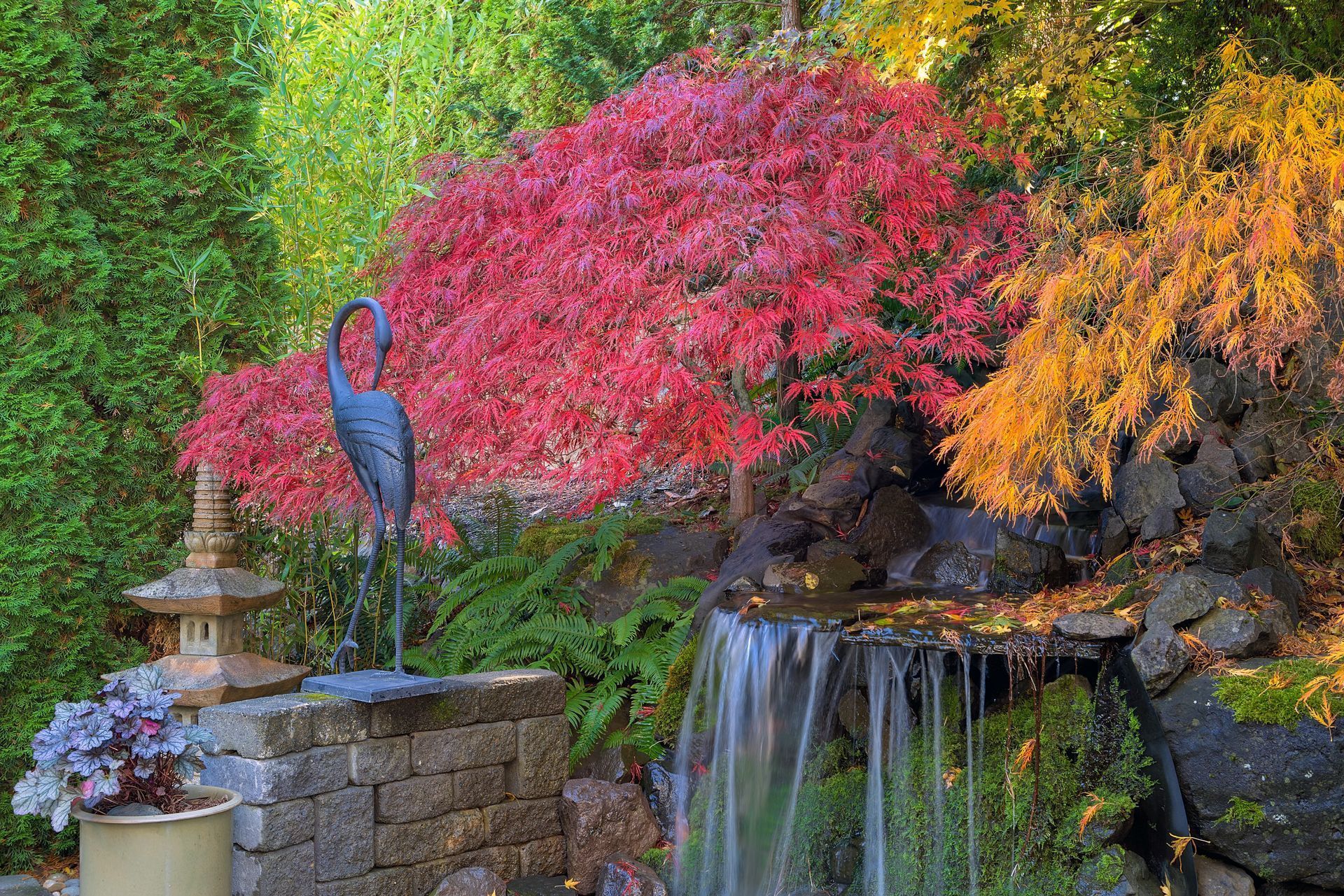 A waterfall in a garden with a bird statue in the foreground.