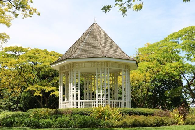 A white gazebo in the middle of a park surrounded by trees.