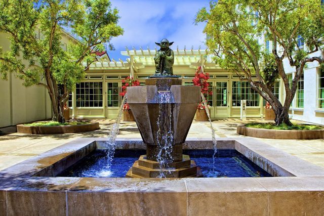 A fountain in a courtyard with trees and a building in the background.