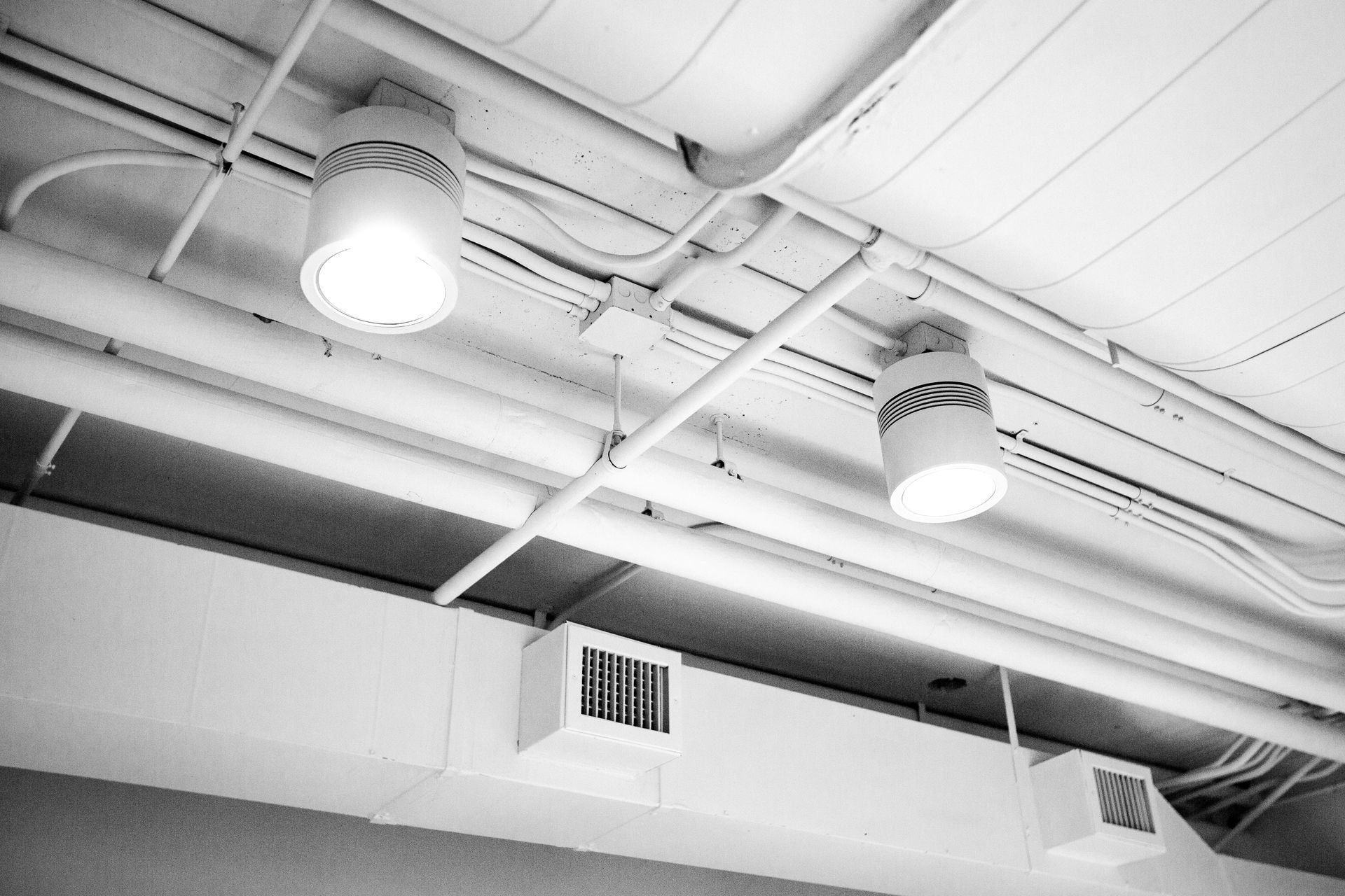 A black and white photo of a ceiling with pipes and lights.