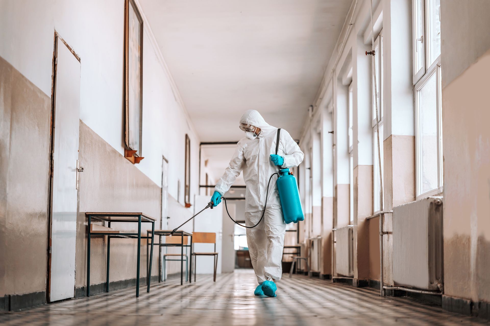 A man in a protective suit is disinfecting a hallway in a building.