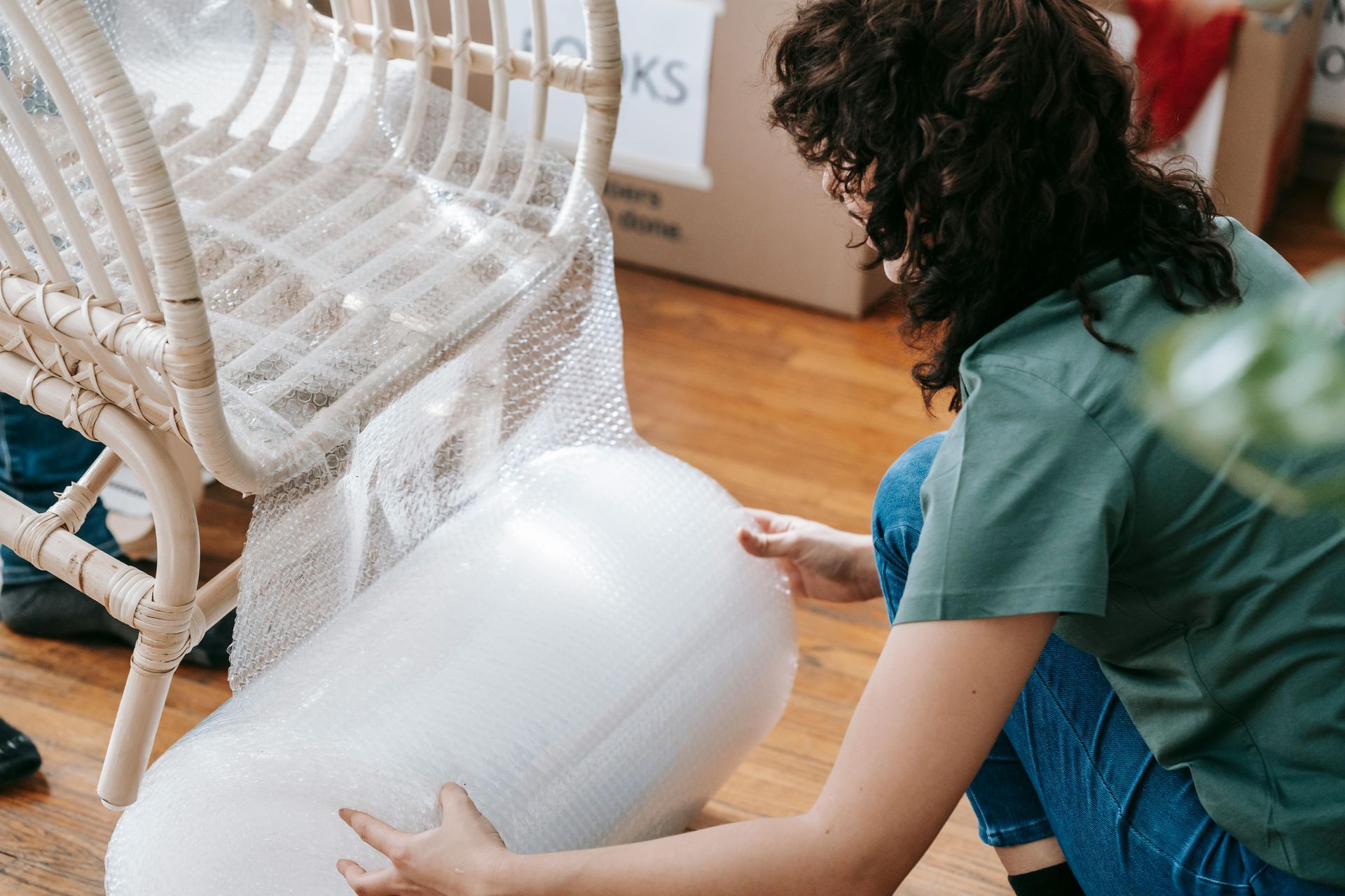 A woman is wrapping a wicker chair with plastic wrap.