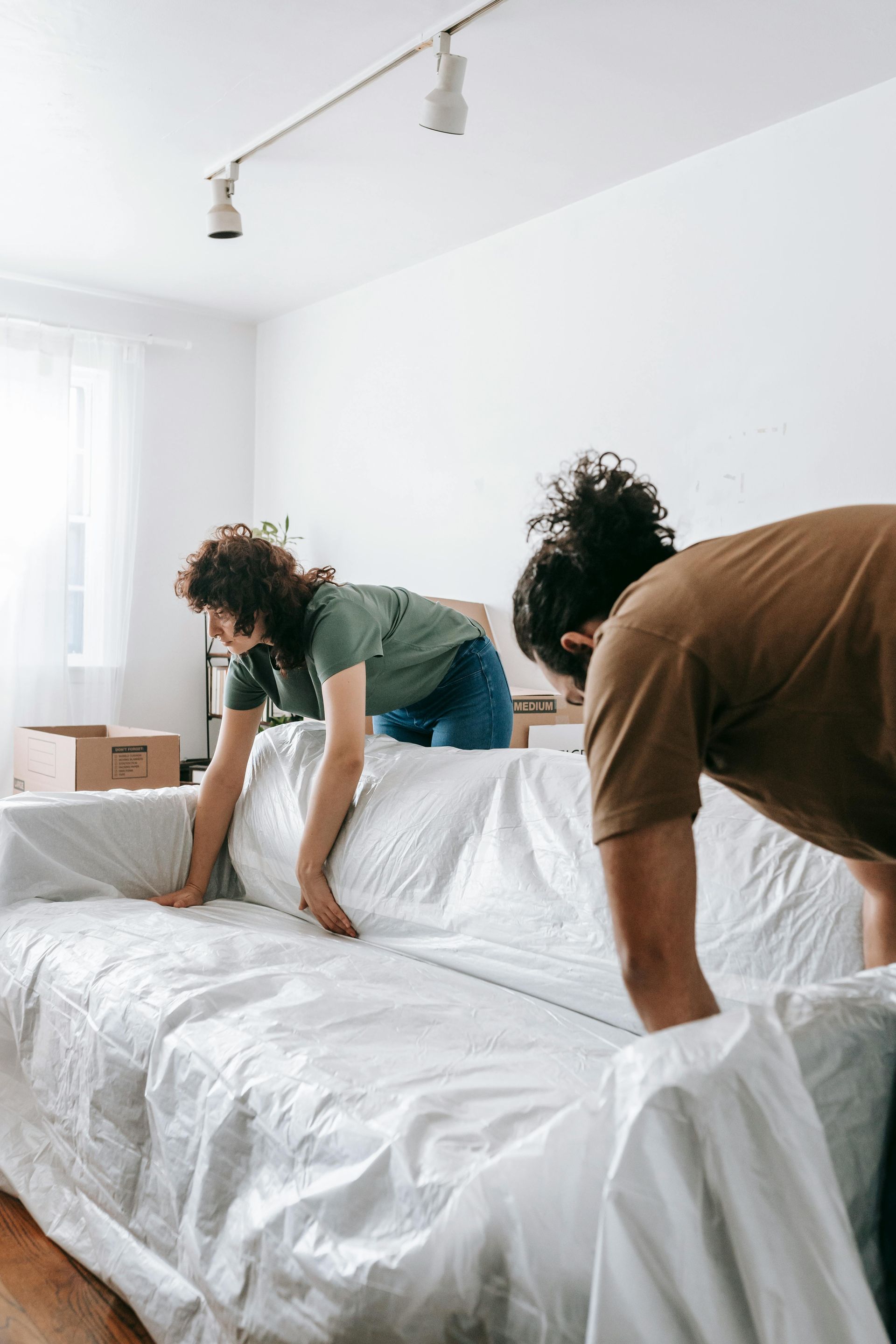 A man and a woman are covering a couch with white sheets.